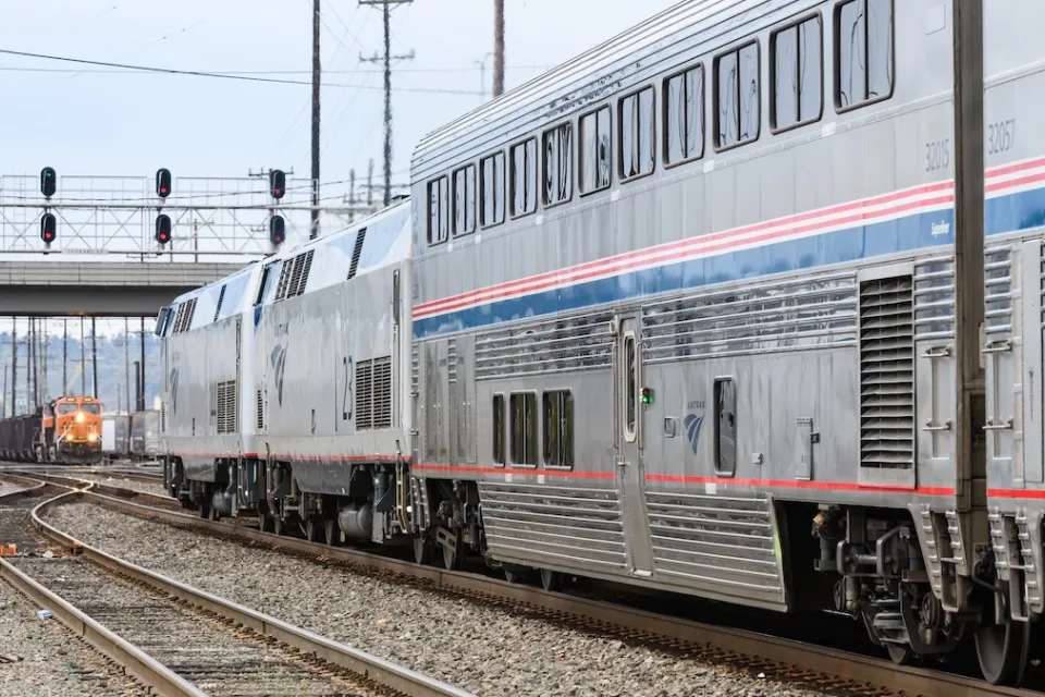 Silver and blue Amtrak train approaching an oncoming orange freight train at station in Seattle, Washington.